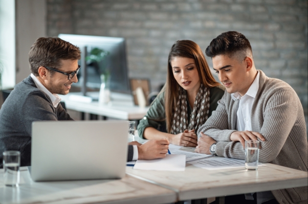 couple sitting at a desk with another man looking at paper work