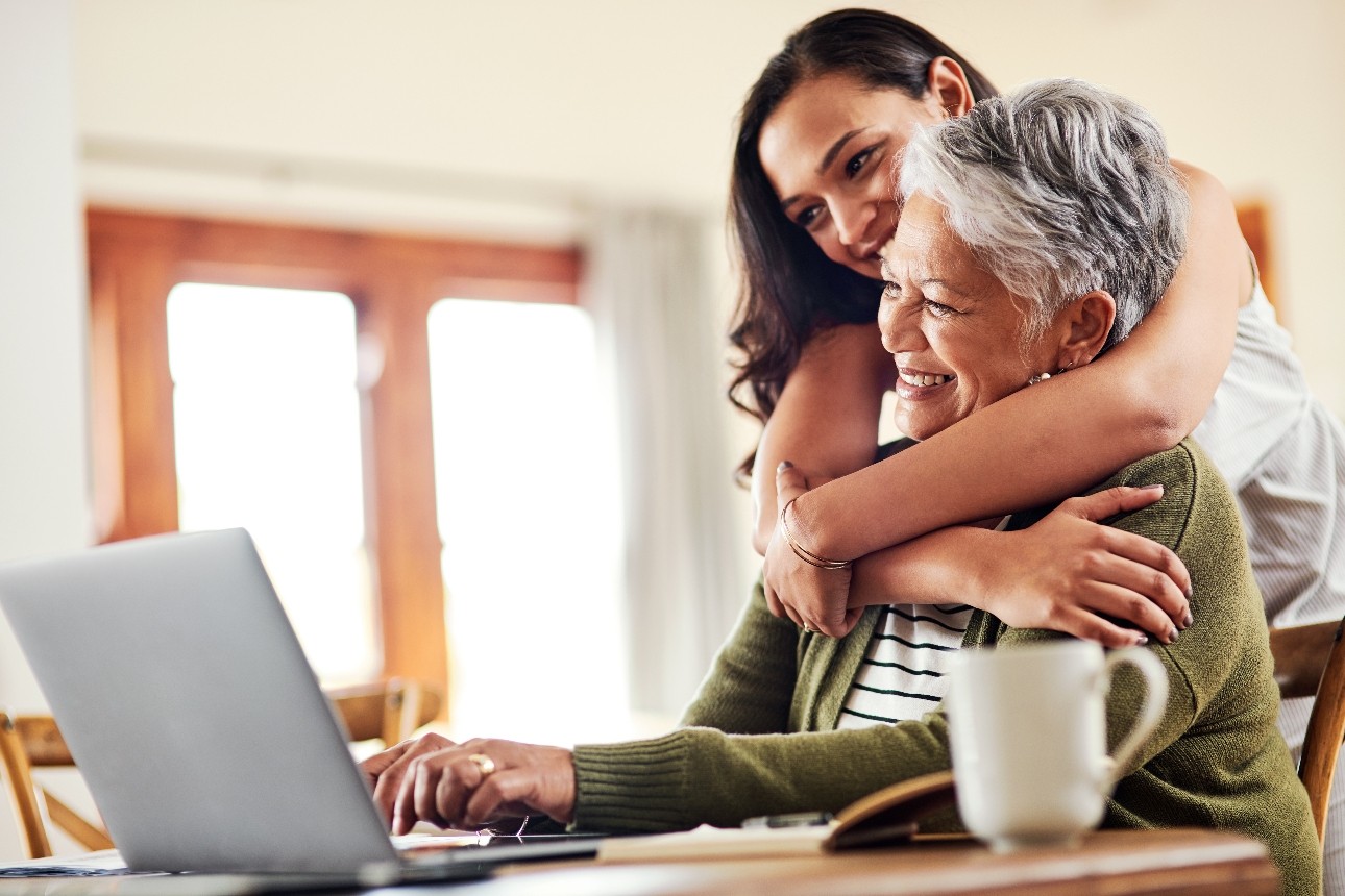 daughter hugging mother at table looking at laptop