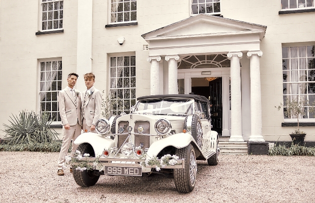 Couple standing outside their wedding venue next to their vintage wedding car