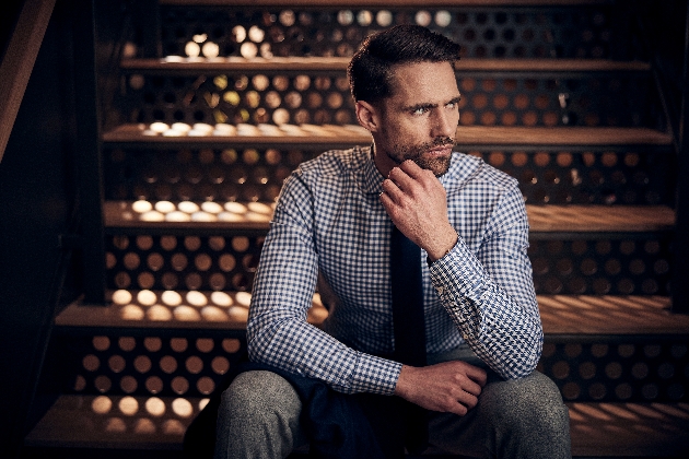 model in checked shirt and grey trousers sitting on the stairs