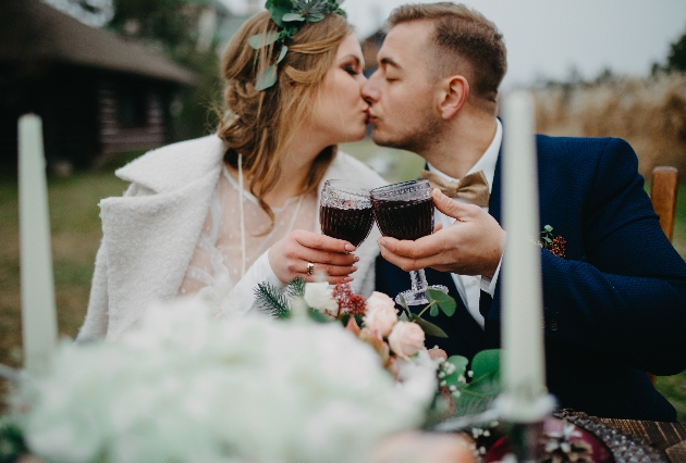 bride and groom in winter wedding outfits drinking red wine outside