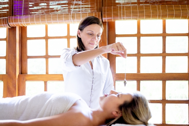 woman laying on a bed with a therapist holding a crystal above her 