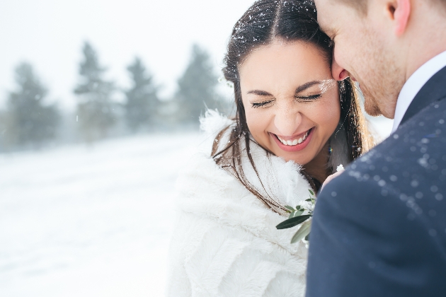 bride snuggled on grooms shoulder with a fur bolero on and snow on her nose