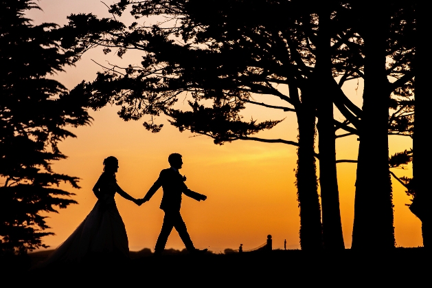 silhouette of bride and groom walking at sunset hand in hand
