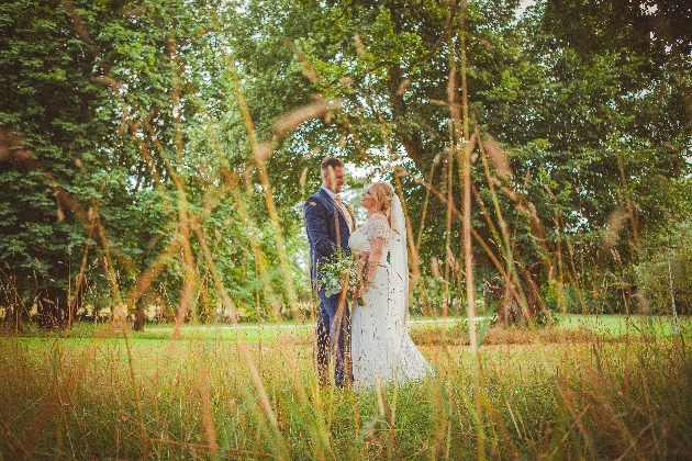 bride and groom in wedding attire standing in the long grass