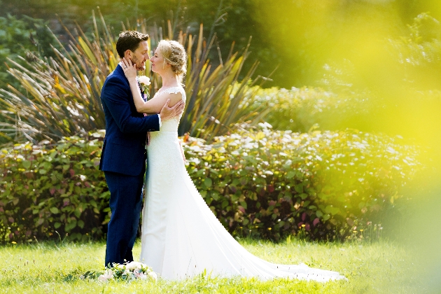 bride and groom in their wedding attire standing on the grass with a bush in the background