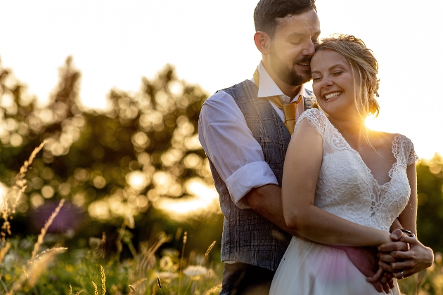 bride and groom in wedding attire hugging with the sun setting in the background 