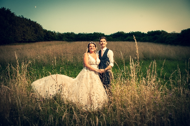 bride and groom in wedding attire standing in a field holding hands 