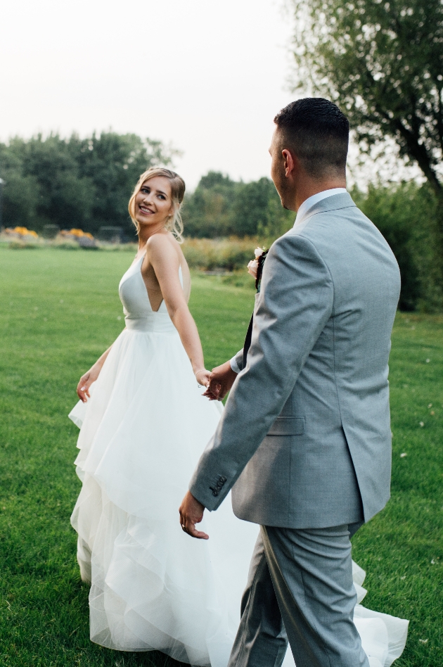 Bride and groom in wedding dress and suit walking through the grounds of their venue holding hands