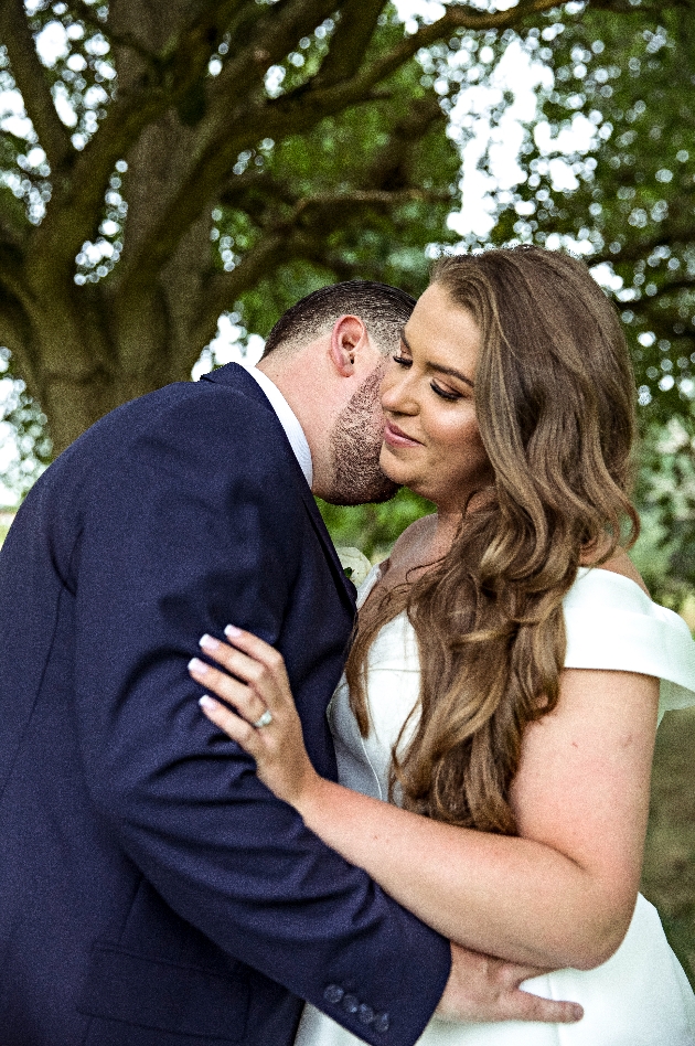 bride in off the should dress getting a kiss of groom in navy suit
