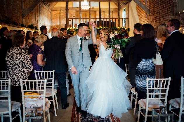 bride and groom walking down the aisle holding hands in the air