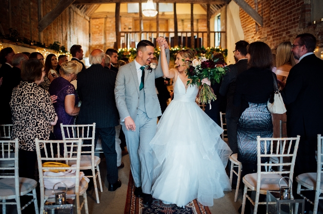 bride and groom walking down the aisle holding hands in the air 