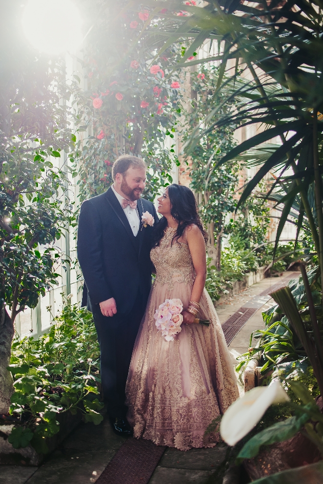 bride and groom in wedding outfits in a botanical garden conservatory lovingly looking at each other