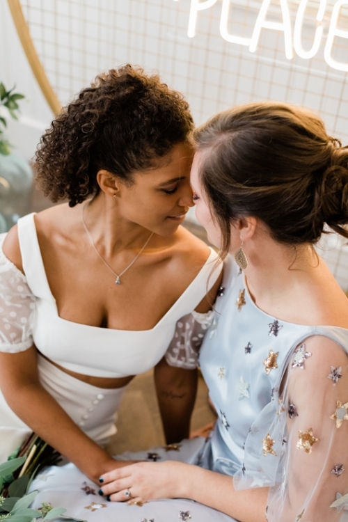 two women in formal wedding attire touching heads in romantic pose