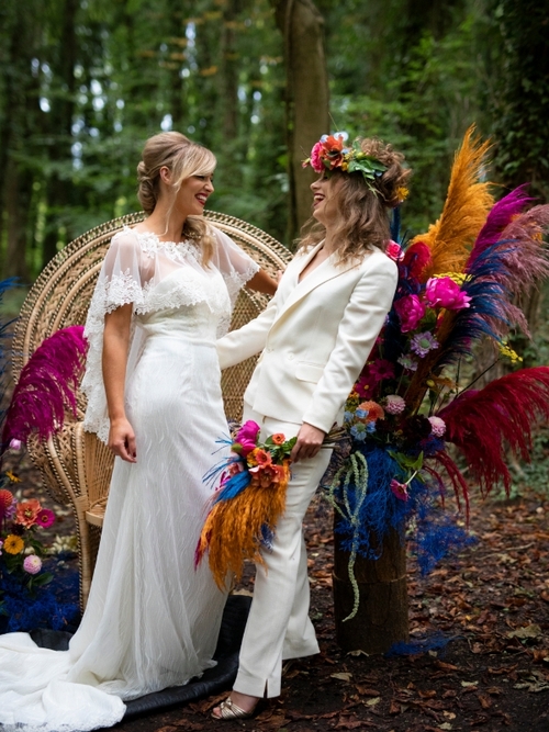 two women one in wedding dress and one in wedding suit having a laugh and holding hands