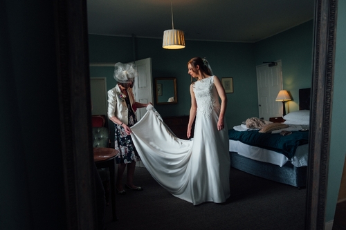 mother of the bride helping the bride in her wedding dress in a green hotel room