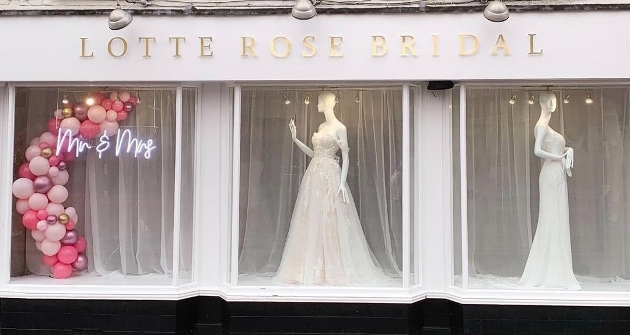 shop front with three large windows, one with balloons and two with dresses