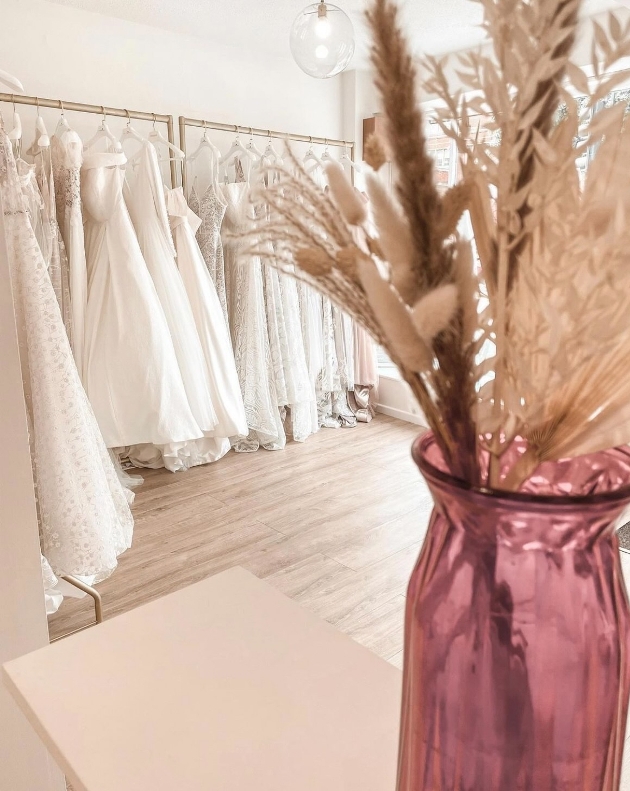 inside a bridal shop with dresses on rails and pink velvet armchair