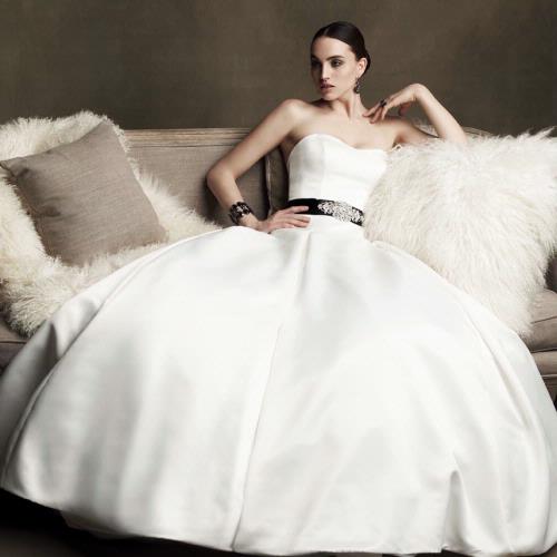 model in a princess style white dress with black belt an sitting on a chair