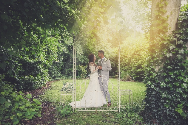 Bride and groom in a garden beneath an arbour
