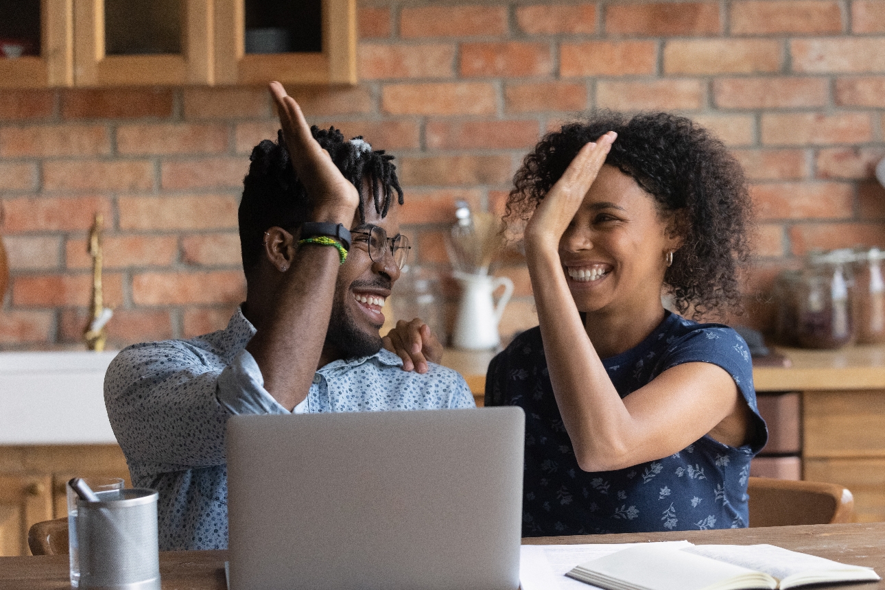 couple at kitchen table at laptop high fiving