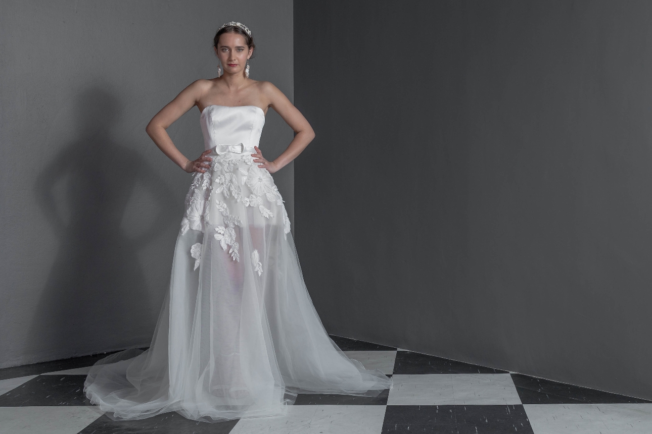 model in strapless corset short dress with sheer long skirt overlay and floral applique around hips