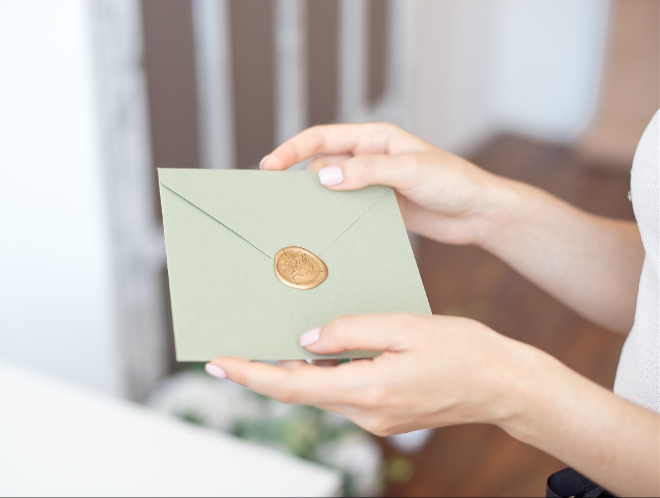 green envelope with gold wax seal being handed to a bride