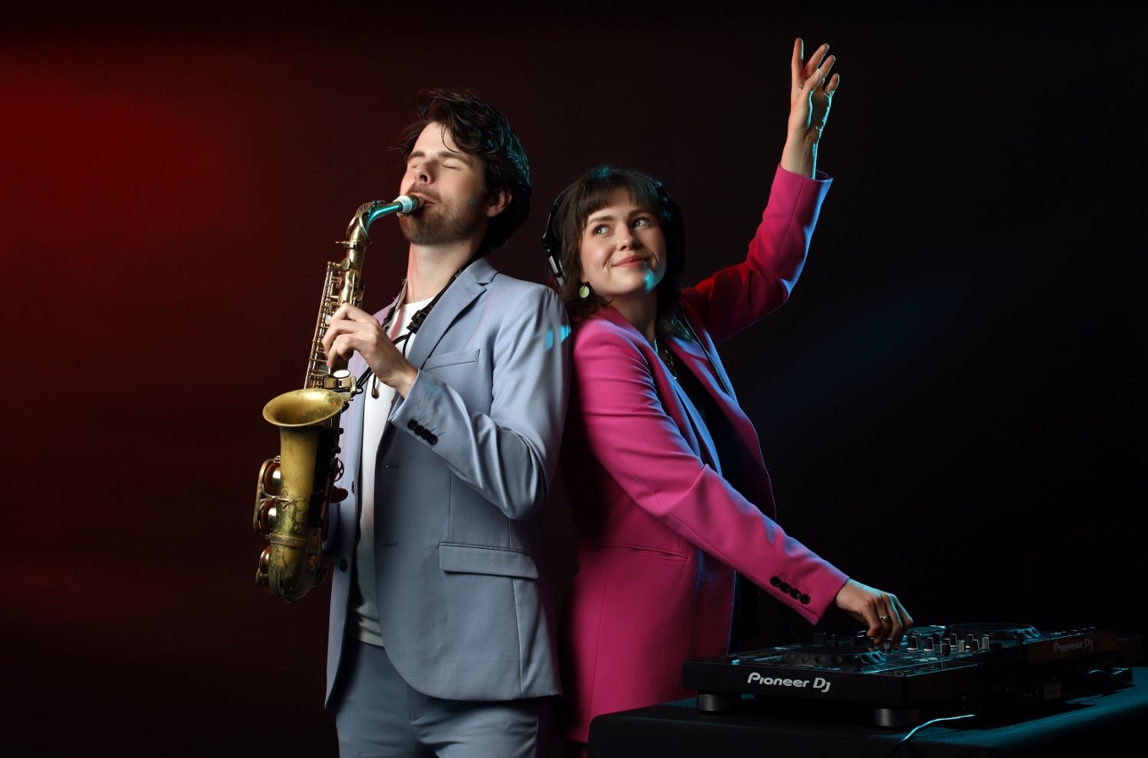 sax player in silver suit, next to DJ in pink suit