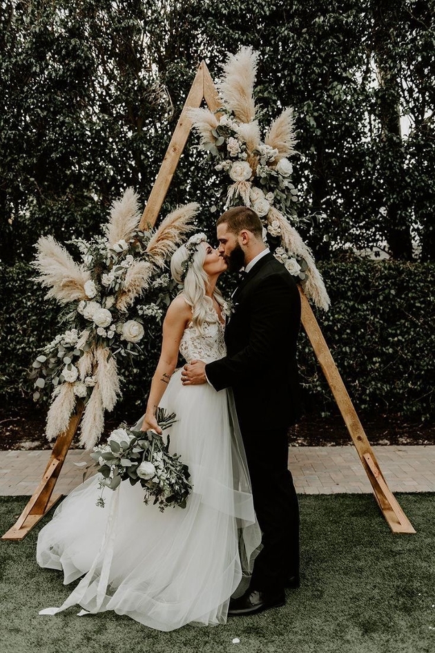 boho bridal couple in front of triangle wooden frame with pampas grass display 