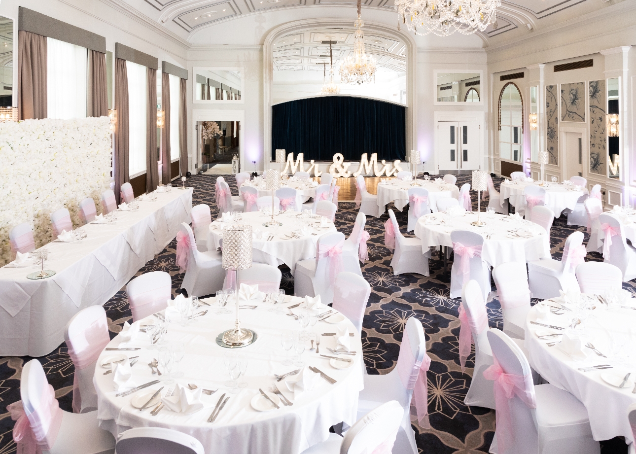 The Castle Hotel reception suite with tables covered in white cloths pink sashes and flower wall